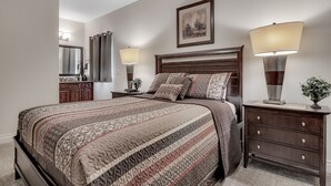 A neatly arranged bedroom with a large bed, two bedside tables, a dresser, a mirror, and a ceiling fan. - Birdie's Paradise 2 Bedroom Villa by RedAwning (Branson)