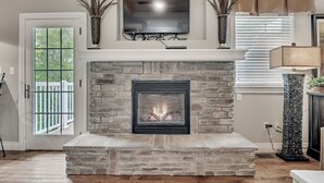 A living room with a stone fireplace, a mounted flat-screen TV, and a door leading to a balcony. - Birdie's Paradise 2 Bedroom Villa by RedAwning (Branson)