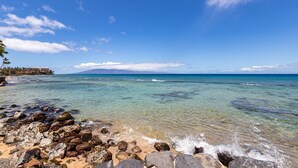 A beach with clear turquoise water, rocky shoreline, and a distant mountain. - Kaleialoha 106 Ocean Front 1bd/1ba 1 Bedroom Condo by RedAwning (Lahaina)