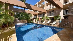 A swimming pool surrounded by palm trees and lounge chairs, with a multi-story building in the background. - Kaleialoha 106 Ocean Front 1bd/1ba 1 Bedroom Condo by RedAwning (Lahaina)
