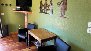 A room with a green wall, a wooden table, two black chairs, a mounted TV, and a decorative wall piece. - Mountain Peaks Inn, GREEN MOUNTAIN SUITE, Downtown Hill City (Hill City)
