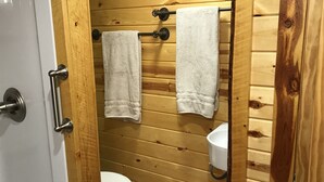 A wooden-paneled bathroom with a toilet, two towels hanging on a rack, and a white sink. - Mountain Peaks Inn, GREEN MOUNTAIN SUITE, Downtown Hill City (Hill City)