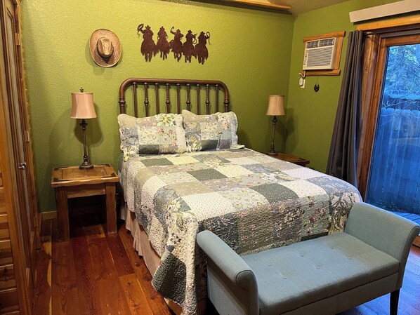 A bedroom with a wooden bed, a quilt, two bedside tables with lamps, a window with curtains, and a green wall.