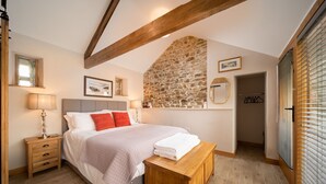 A bedroom with a stone wall, a bed with a wooden headboard, a bedside table, and a bench. - Charming countryside cottage for couples with private hot tub and communal games room. (Barnstaple)