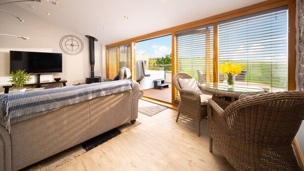 A modern living room with a sofa, a TV, a fireplace, and a balcony with outdoor furniture. - Charming countryside cottage for couples with private hot tub and communal games room. (Barnstaple)