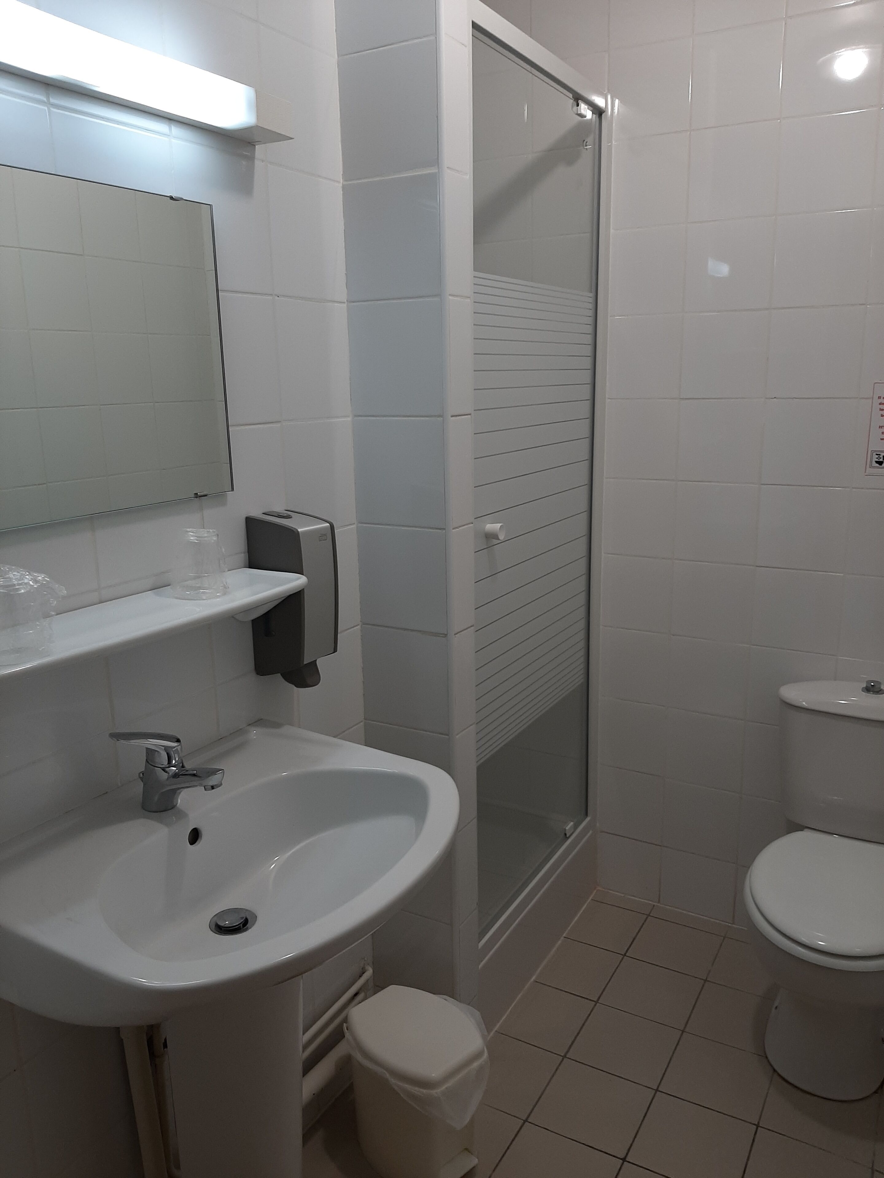 Et badeværelse med vask, toilet og et brusekabine med glasvægge.