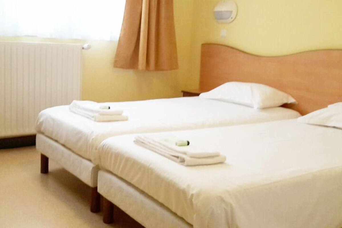 A hotel room with two single beds, each with a white duvet and a folded towel.