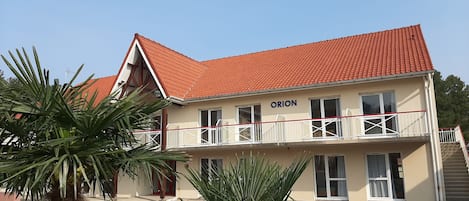 Un edificio de dos pisos con techo de tejas rojas y el nombre 'ORION' en la fachada.