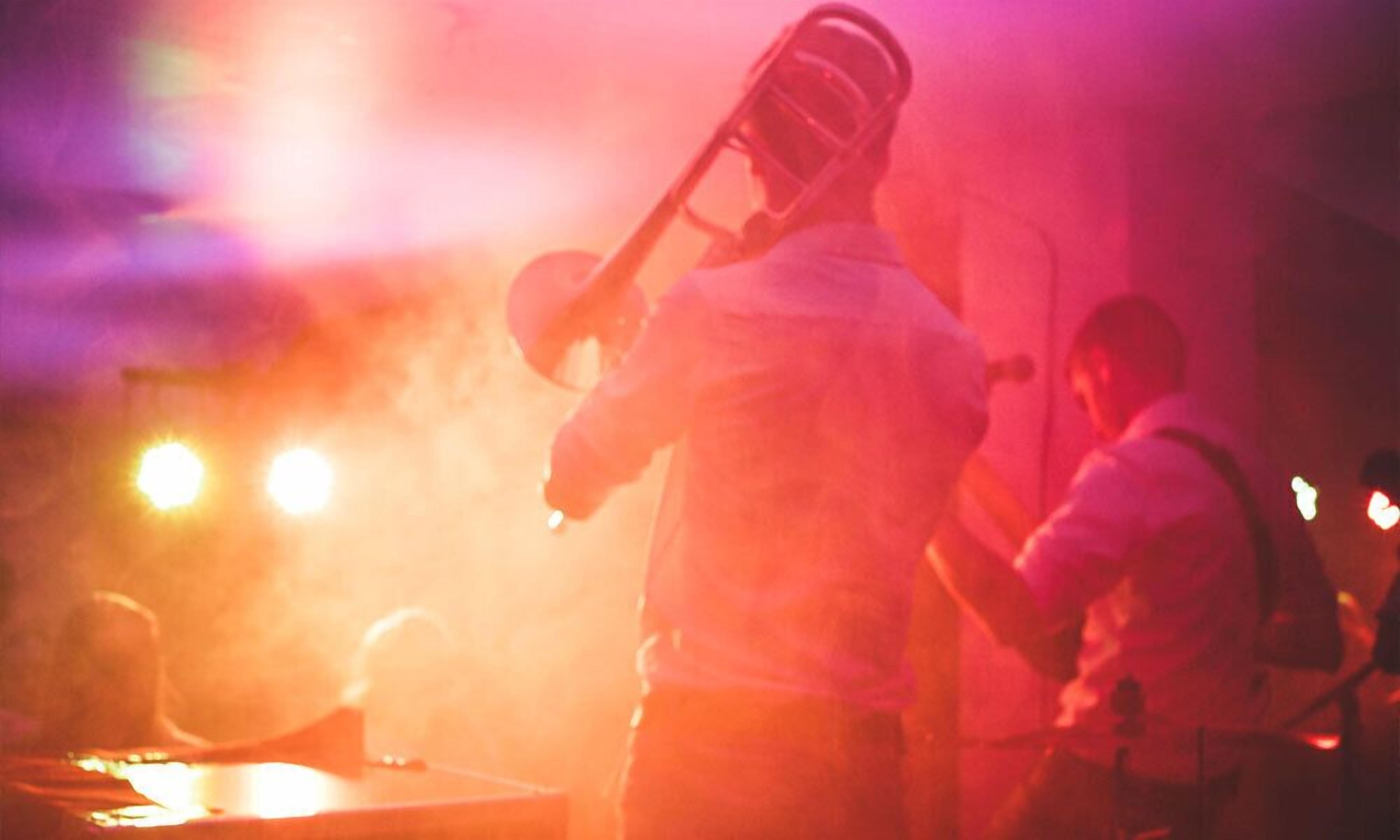 A person playing a brass instrument, likely a trumpet, in a dimly lit setting with warm lighting.