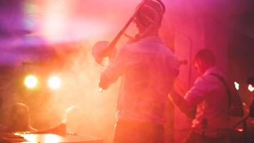 A person playing a brass instrument, likely a trumpet, in a dimly lit setting with warm lighting.