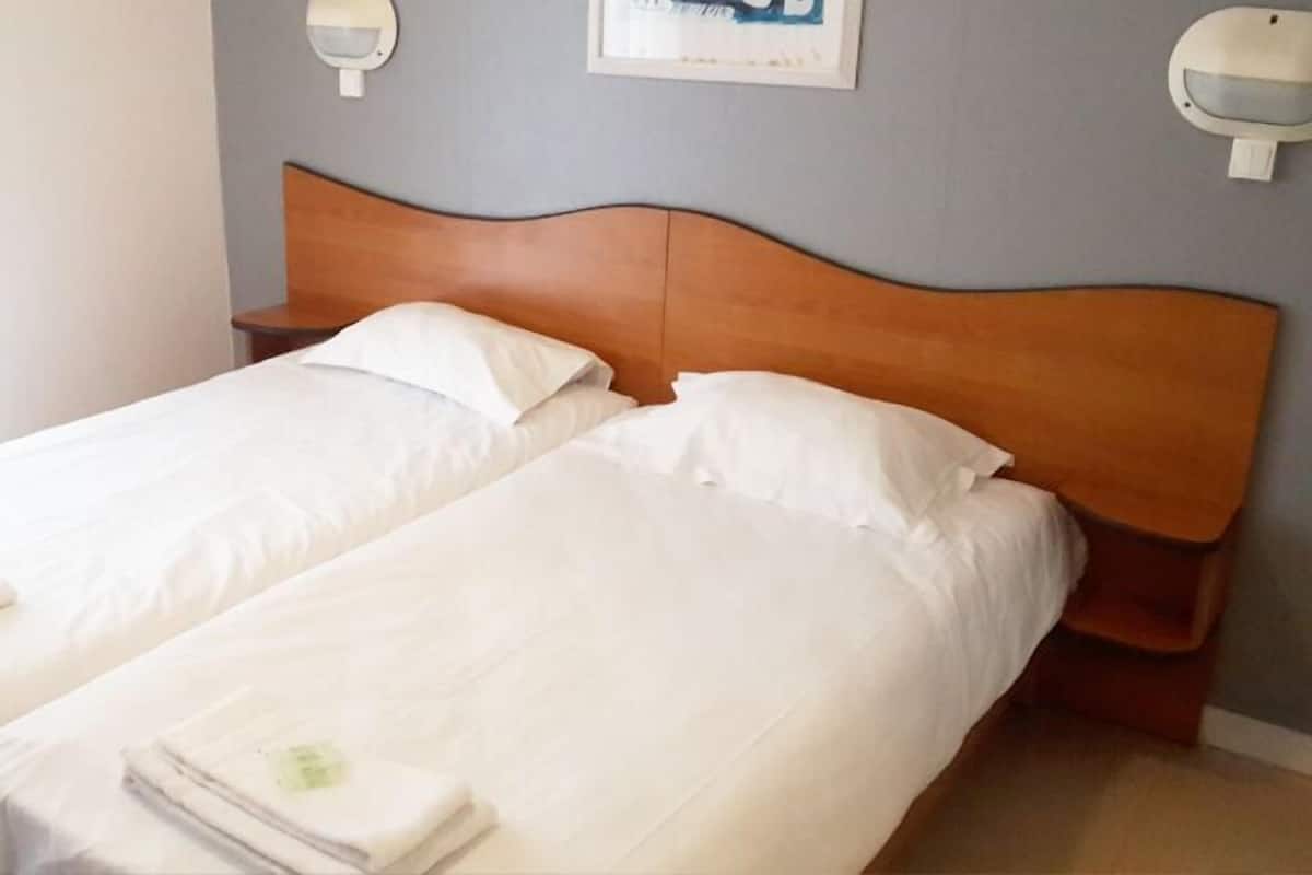 A double bed with a wooden headboard, white linens, and a small bedside table with a lamp.
