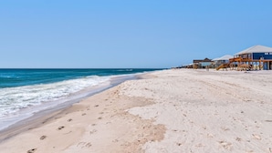 Una spiaggia con impronte che conducono a un'area con un pontile di legno e edifici sullo sfondo.