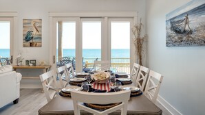 Zona pranzo con vista sull'oceano, arredi bianchi e opere d'arte a tema nautico.
