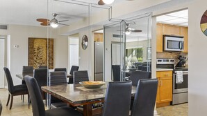 Une cuisine moderne équipée d’appareils électroménagers en acier inoxydable, un coin repas avec une table en marbre et un ventilateur de plafond.