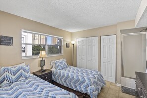 A bedroom with two beds, a window with a city view, a lamp, and a closet. - Walk to the Beach at Sunny Isles (Sunny Isles Beach)