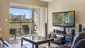 Un salon avec une table en verre, un canapé, un téléviseur et un balcon aménagé avec du mobilier d’extérieur.