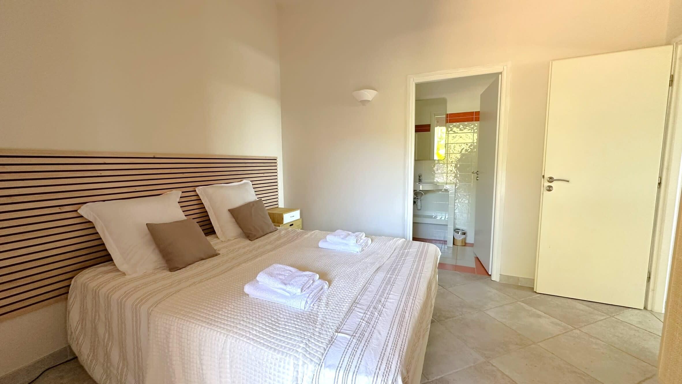 A neatly made bed with a striped headboard, a bedside table, and a bathroom visible through an open door.