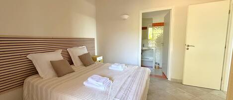 A neatly made bed with a striped headboard, a bedside table, and a bathroom visible through an open door.