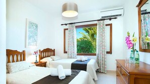 A hotel room with two beds, a wooden dresser, a nightstand, a lamp, and a window with curtains. - Villa Geranios, country house a few minutes driving from Pollensa (Pollença)