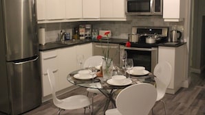A modern kitchen with white cabinets, a stainless steel refrigerator, a microwave, and a stove. There is a dining table with chairs and a vase with flowers.