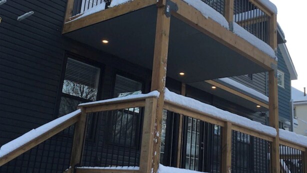 A multi-story building with a wooden balcony railing and snow on the ground.
