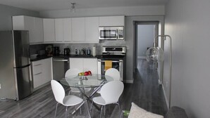 A modern kitchen with white cabinets, stainless steel appliances, a glass dining table with white chairs, and a microwave above the stove.