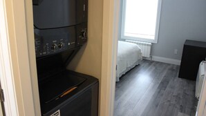 A compact room with a built-in washer and dryer, a bed with a white bedspread, and a radiator under a window.