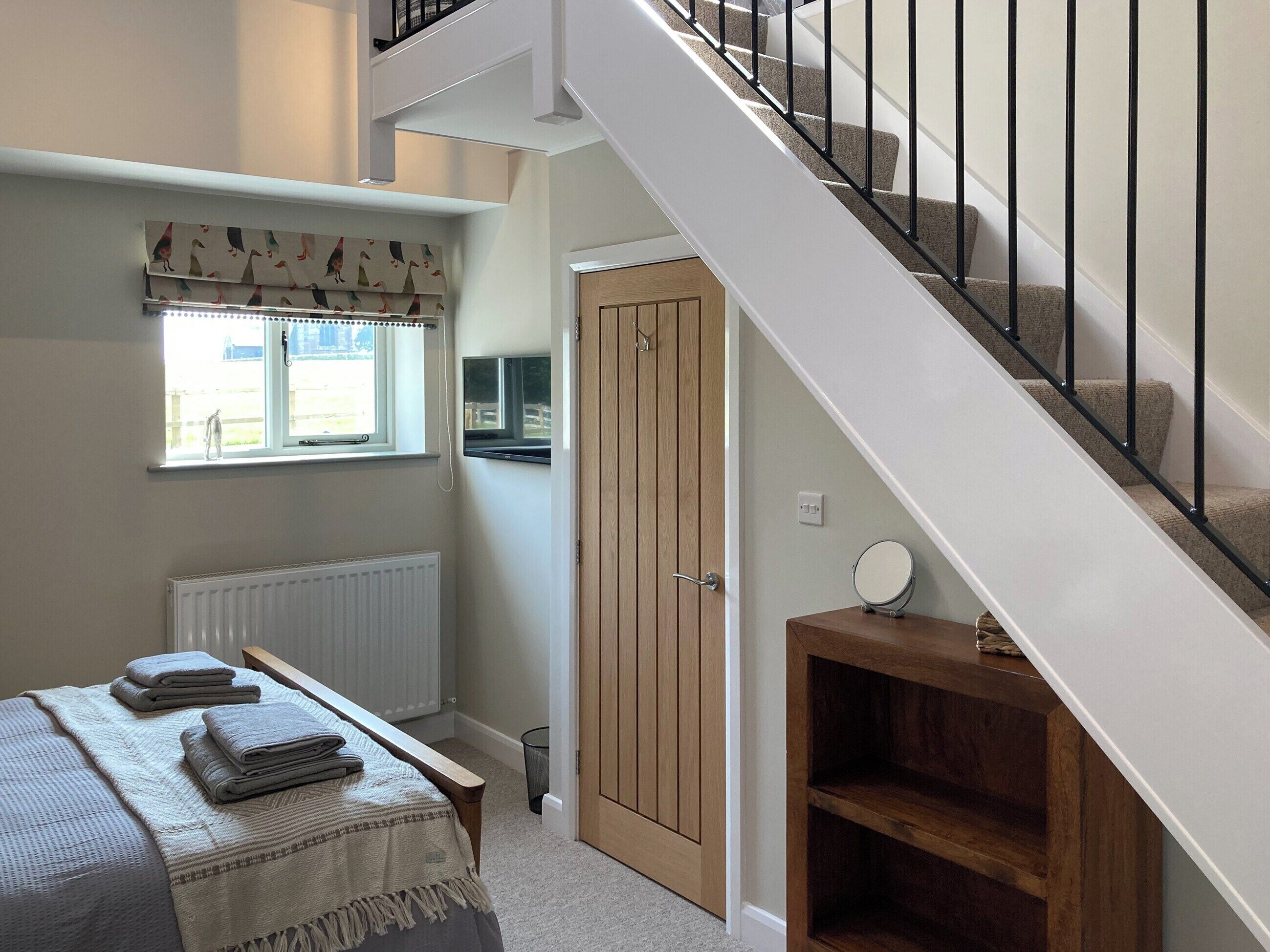 A bedroom with a bed, a window, a radiator, a wooden door, and a staircase.