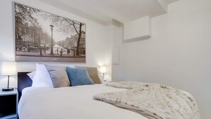 Ett hotellrum med en säng, ett nattduksbord, en lampa och en tavla som hänger på väggen.