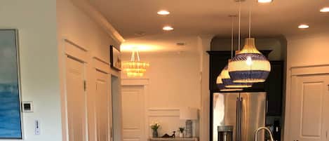 A modern kitchen with a central island, bar stools, pendant lighting, and a dining area with a round chair and cushions.