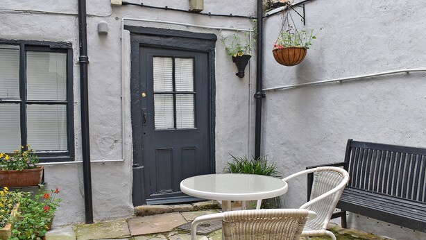 A courtyard with a black door, white wicker chairs, a round table, and potted plants.