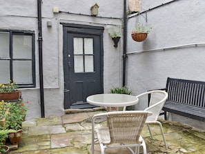 A courtyard with a black door, white wicker chairs, a round table, and potted plants.