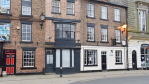 A row of traditional brick buildings with multiple windows and doors, including a pub with a black awning and a sign for 'Café Di Lucca'.