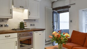 A compact kitchen with white cabinets, a stove, and a built-in oven. There's a wooden table with a vase of flowers and an orange sofa in the living area.