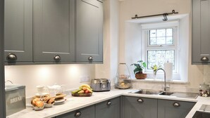 Een moderne keuken met grijze kastjes, een marmeren aanrechtblad, een inbouwoven en een raam met uitzicht op groen.