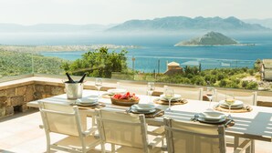 A dining table set outdoors with a view of the sea and mountains. - Villa Tzikides Aegina (Aegina)