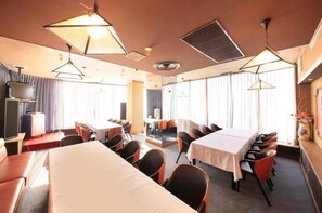 Una habitación de hotel con una cama grande, un escritorio, un televisor y un área de comedor con mesas y sillas.