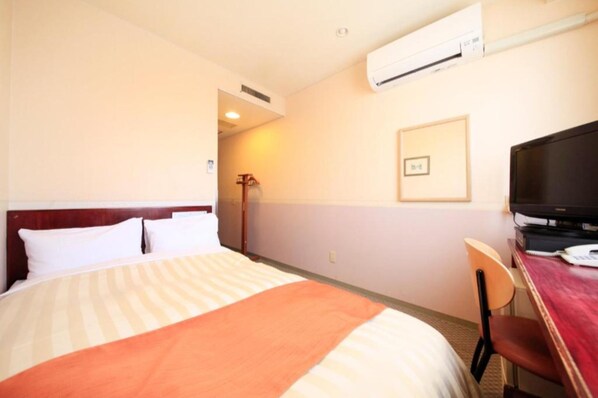 Ein Hotelzimmer mit Bett, Schreibtisch, Stuhl, Fernseher und Klimaanlage.