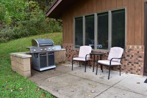 Un patio exterior con una parrilla, dos sillas y una mesa.