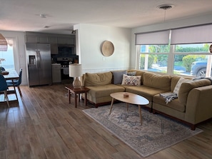 A modern living room with a sofa, coffee table, and rug, a kitchen with appliances, and a dining area with chairs. - Canal front home on Longboat Key -Just Steps to the Beach (Longboat Key)