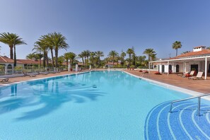A swimming pool with lounge chairs and palm trees. - Bungalow Sun Club OS55 by VillaGranCanaria (Playa del Ingles)