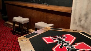 A bar area with a black counter, two stools, a TV screen, and a red and black table with a logo. - Sportsman's Country Lodge: The Fish House (Webster)