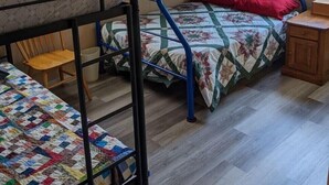 A dormitory room with bunk beds, a wooden chair, a small table, and a window with blinds. - Sportsman's Country Lodge: The Fish House (Webster)