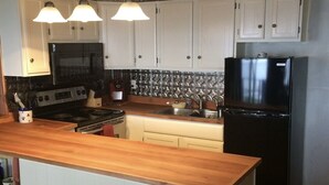 A kitchen with white cabinets, a black refrigerator, a wooden countertop, and two pendant lights.