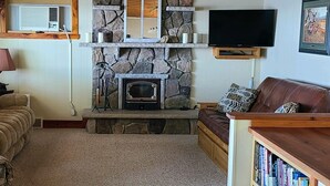 A cozy living room with a stone fireplace, a television mounted on the wall, and a leather sofa.