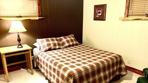 A bedroom with a bed, a nightstand, a lamp, a framed picture on the wall, and a window with blinds.