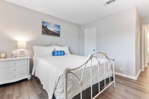 A bedroom with a white bed, a nightstand with a lamp, and a picture on the wall. - Water View - optional BIKES - Walk 2 Pier Village (St. Simons Island)