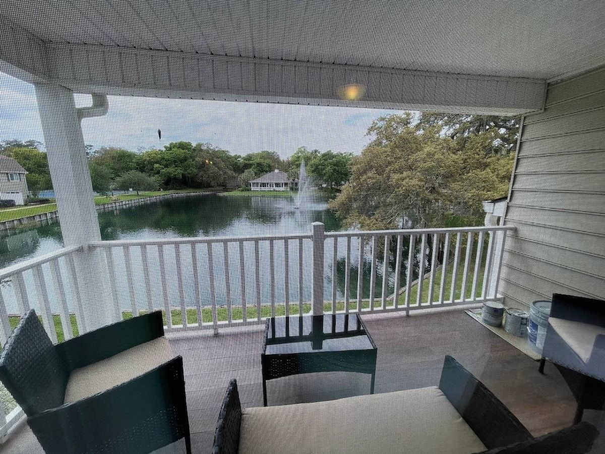 A balcony with a view of a fountain and trees, furnished with chairs and a table.
