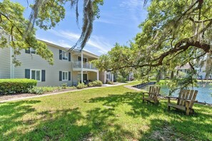 A two-story building with a balcony, a grassy lawn, and a body of water. - Water View - optional BIKES - Walk 2 Pier Village (St. Simons Island)