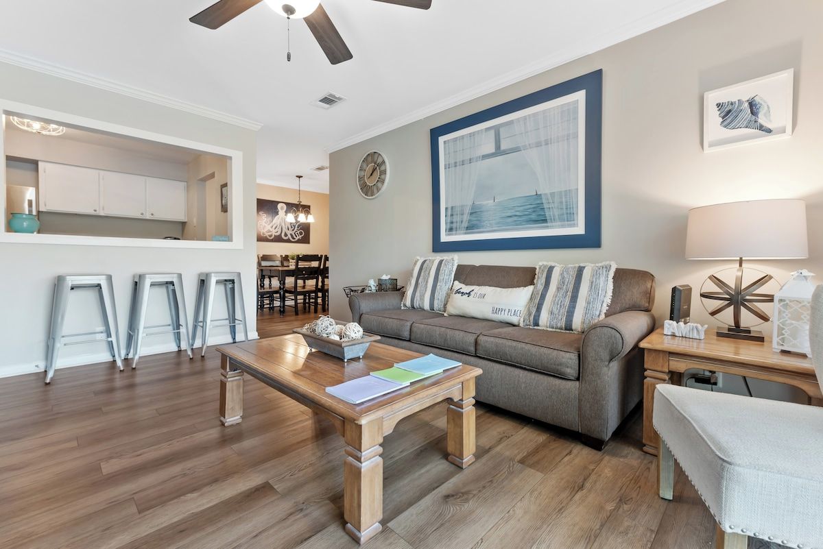A living room with a sofa, coffee table, and a dining area with stools.